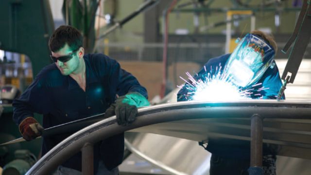 Two workers in protective gear welding a metal structure, with bright welding sparks.