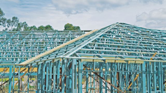 Timber house frames under construction with roof trusses and wall framing visible.