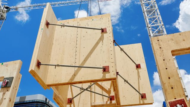 Large engineered timber panels being lifted by a crane at a construction site.