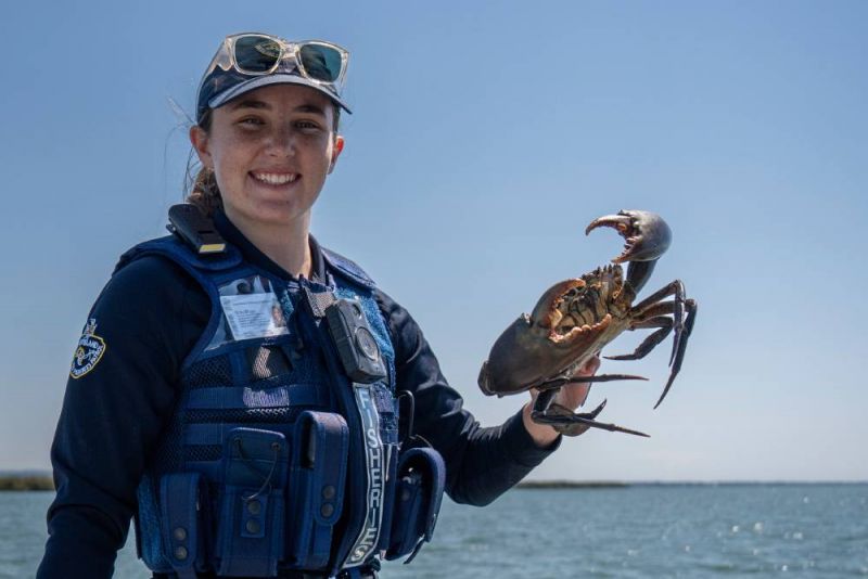 A young female fisheries patrol officer holding up a crab. 