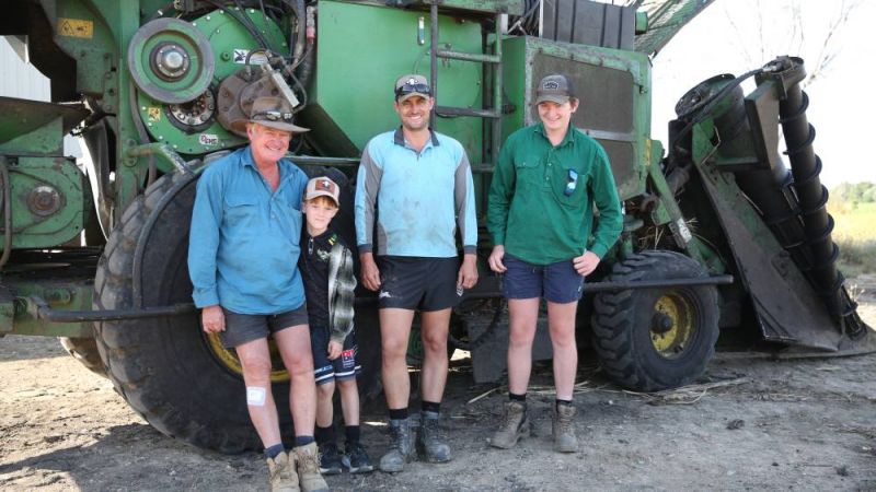 A grandfather, son and two grandsons standing in front of a sugarcane tractor.