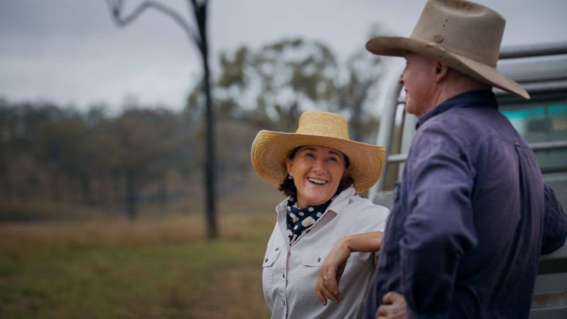 A woman and man wearing akubras leaning on a truck in a bush setting.