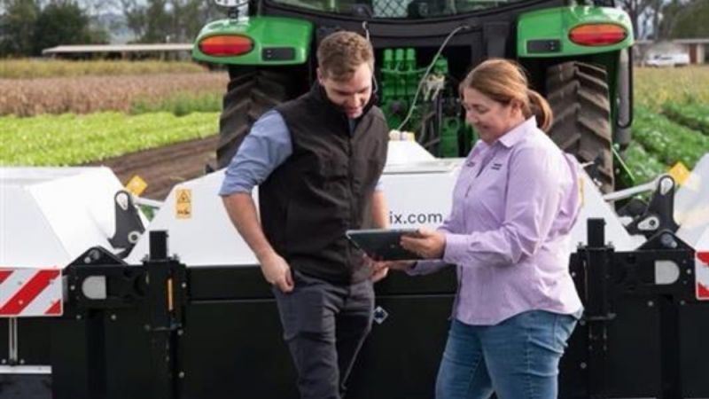 A man and woman in a field standing in front of an automonous robot.